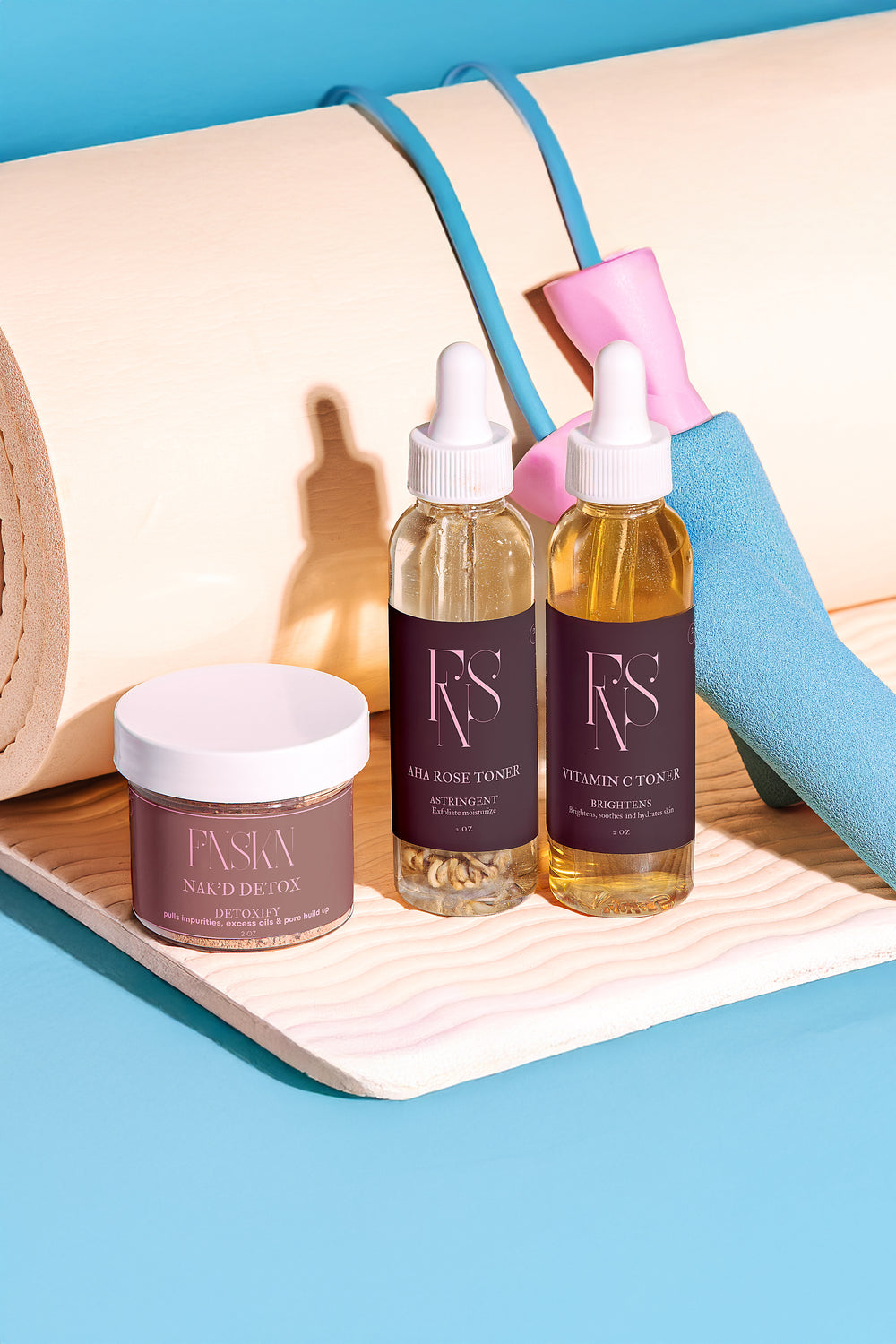 Faska skincare products including a jar, two bottles, and a spray bottle on a wooden tray with a blue background.