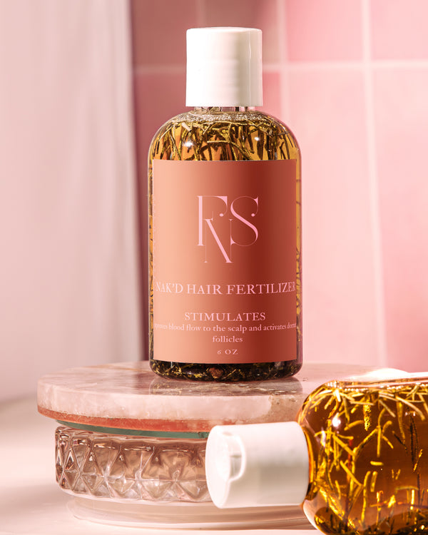 A bottle of Nak’d Growth Hair Fertilizer placed on a round glass object with a pink background. The bottle is adorned with a brown label and contains a yellow liquid.