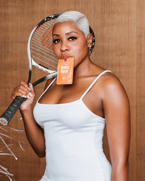 Woman holding a tennis racket and a Nutri-bay snack in front of her mouth against a wooden background